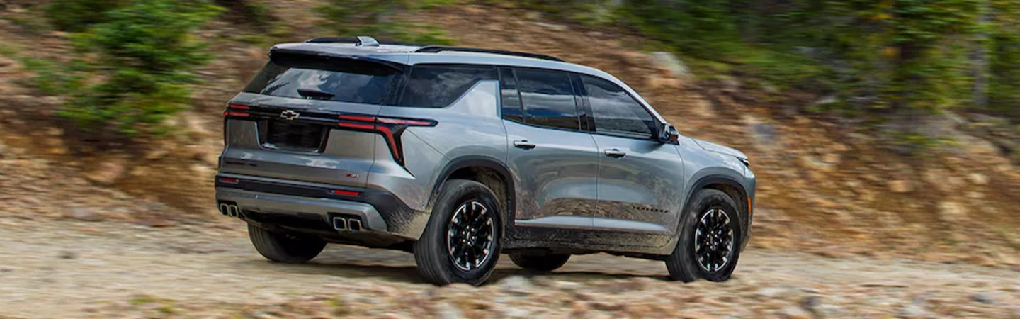 Side back view of a 2024 Chevrolet Traverse driving on a dirt road