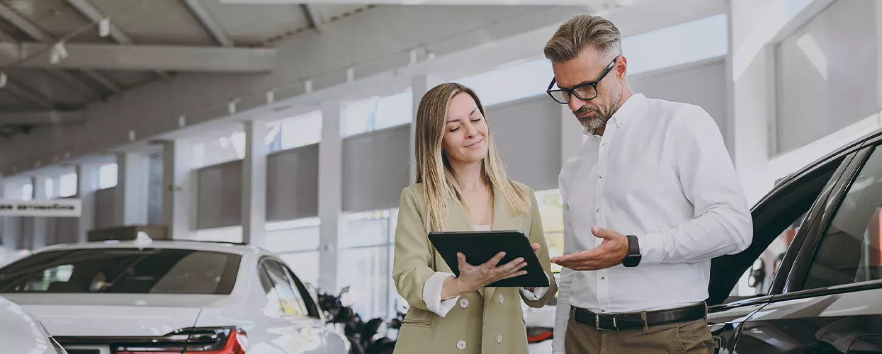Car sales woman showing a man a clipboard in a car dealership
