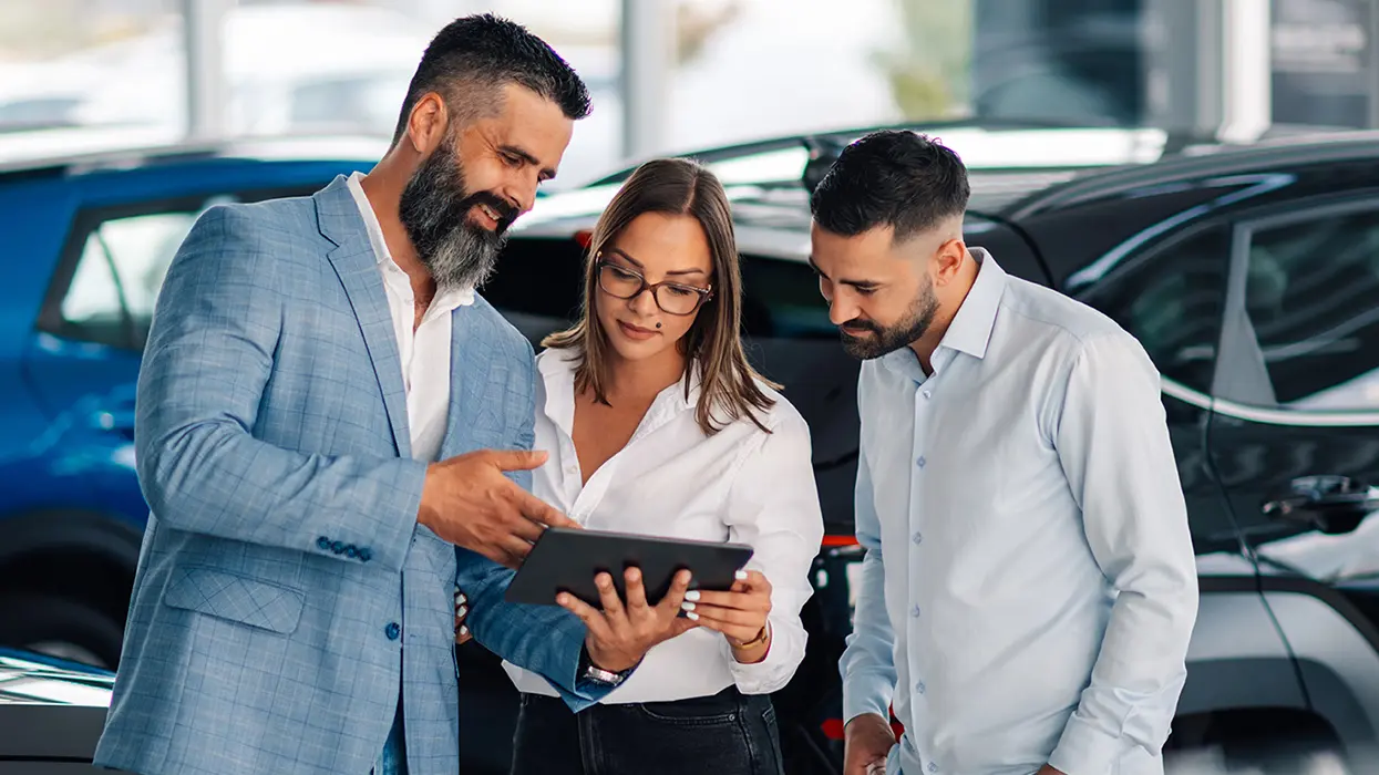 car salesperson showing another person specification on a new car purchase in the deaership showroom