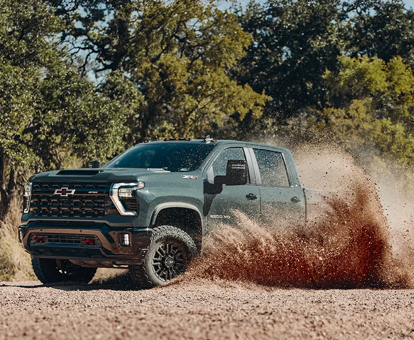 Front side view of a green 2026 Chevrolet Silverado 2500 HD driving around in dirt