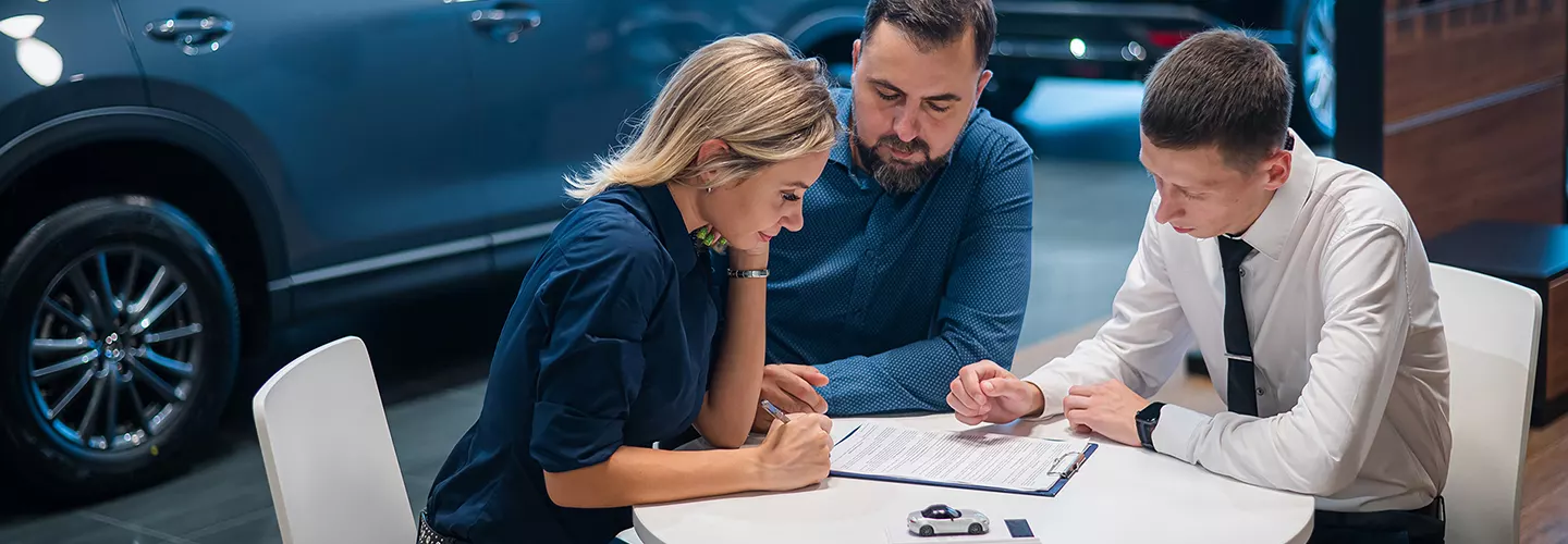Three people sitting at a table at a car dealership talking about a contract