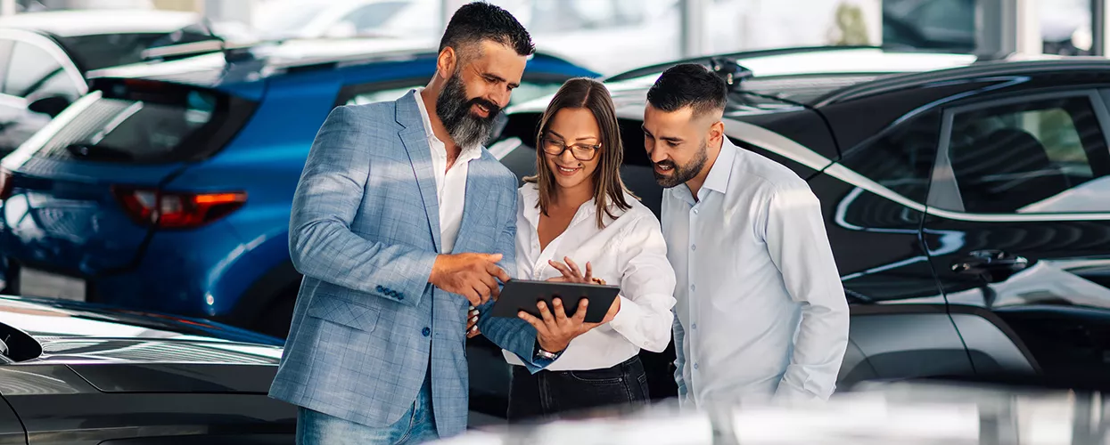 Three people looking at a tablet in a car dealership