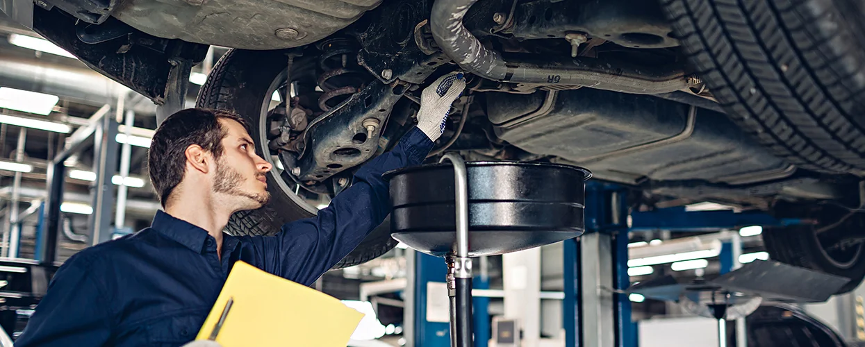 auto mechanic working on car on a lift changing fluids