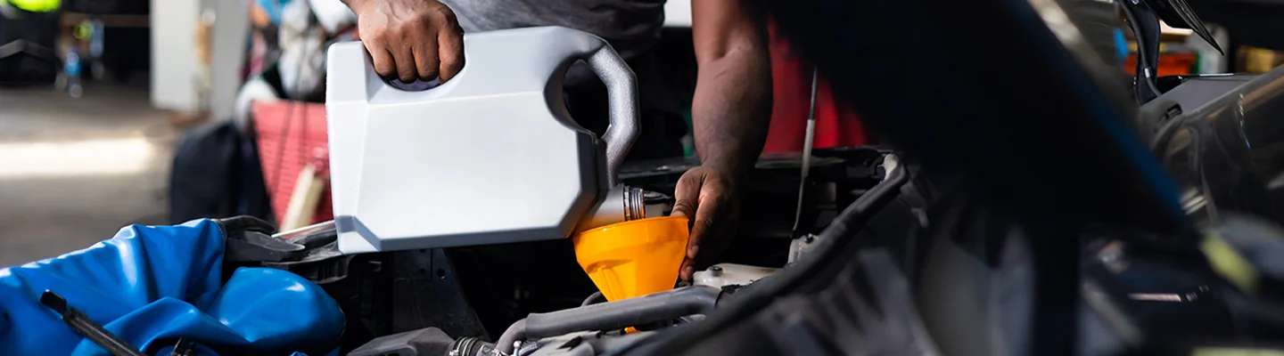 auto mechanic pouring oil into engine