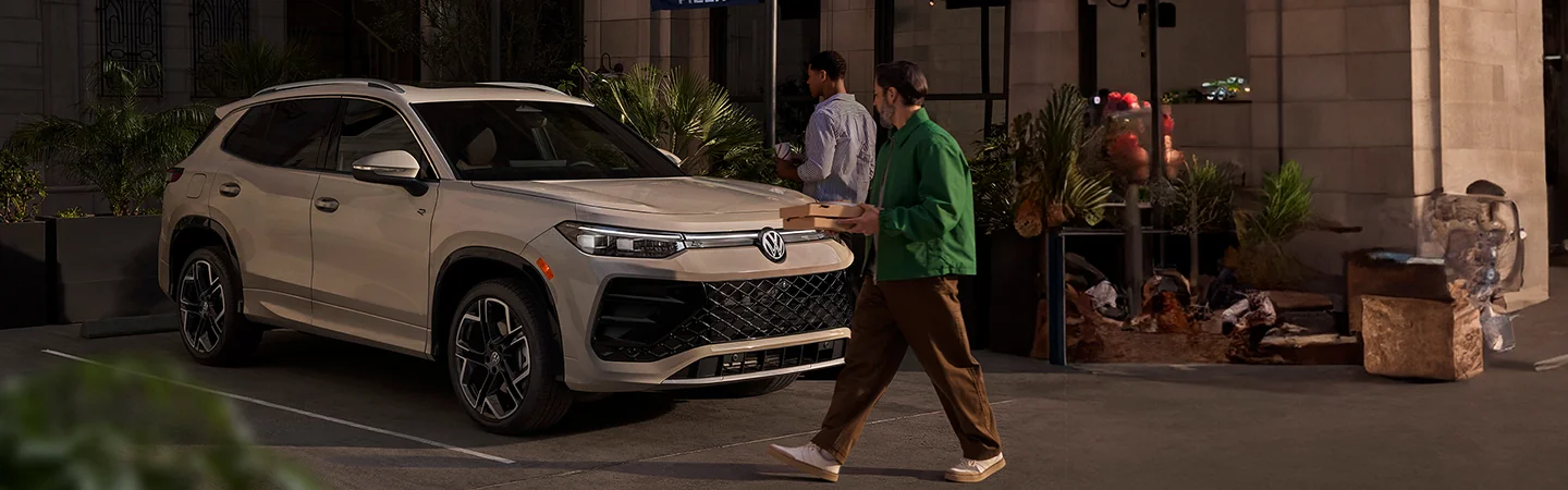 two people approching a 2025 Volkswagen Tiguan S with food in hand