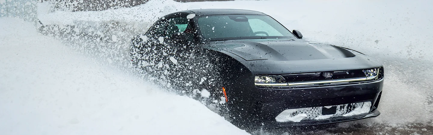 Front side view of a black 2025 Dodge Charger driving though the snow