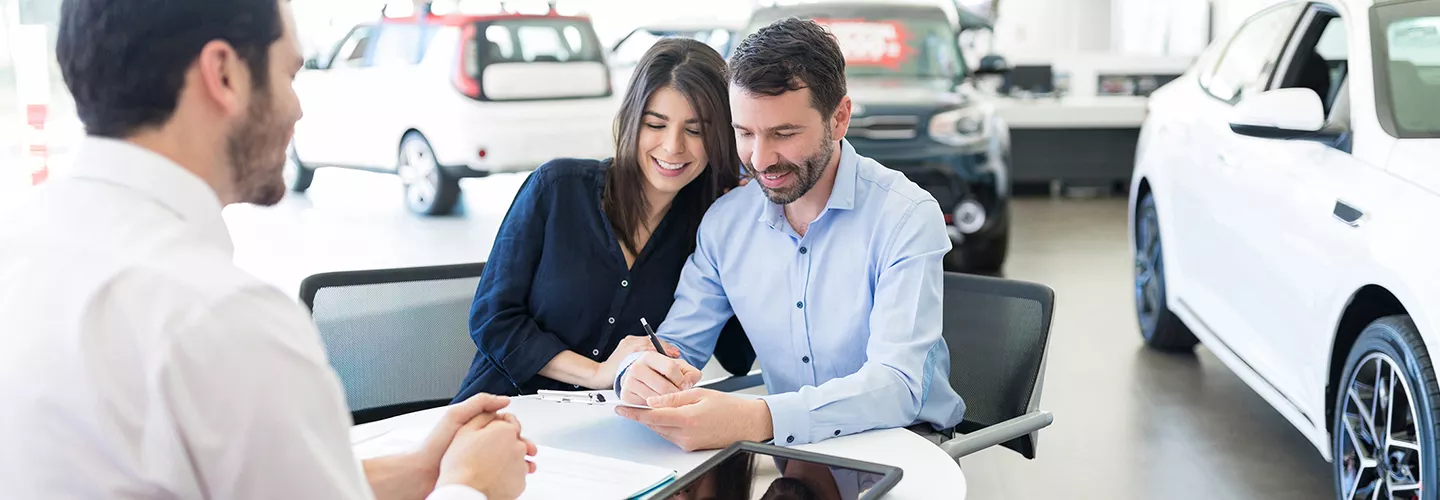 Couple signing a document at a car dealership