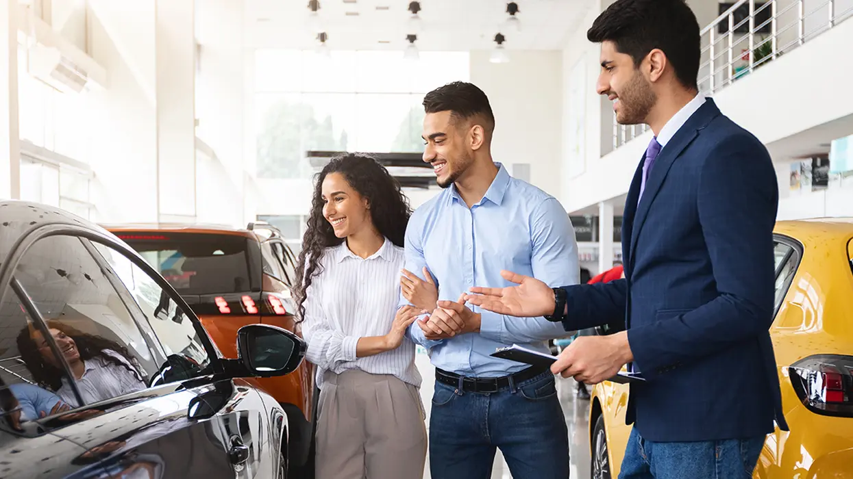 car salesperson showing another person specification on a new car purchase in the deaership showroom