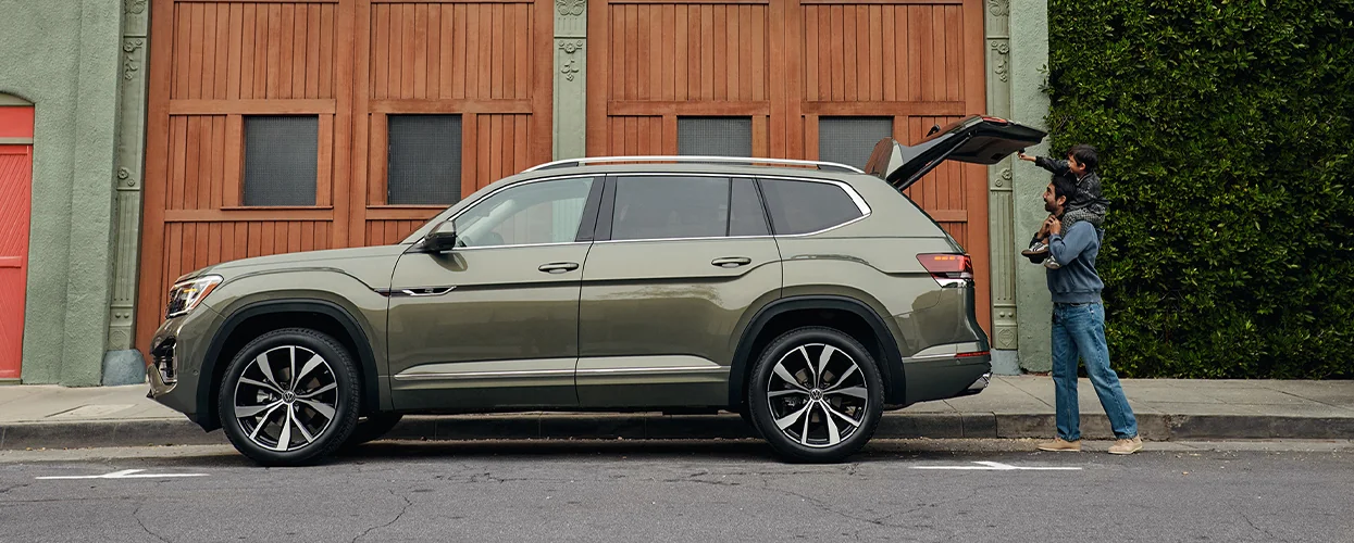 Side view of a father and son closing the truck of their green 2026 Volkswagen Atlas