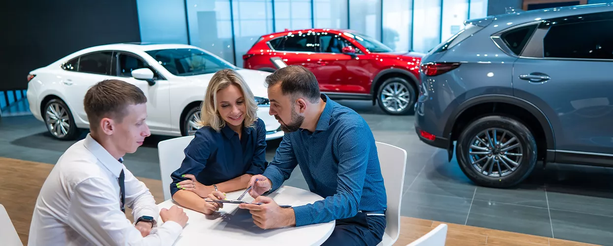 Three people sitting at a table in a car dealership