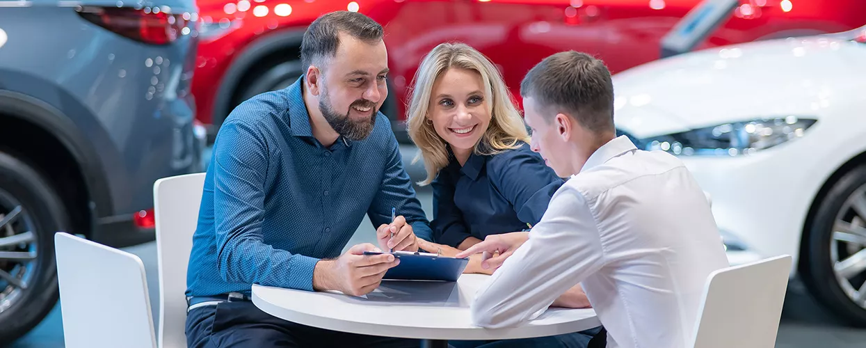 Three people sitting at a table in a car dealership