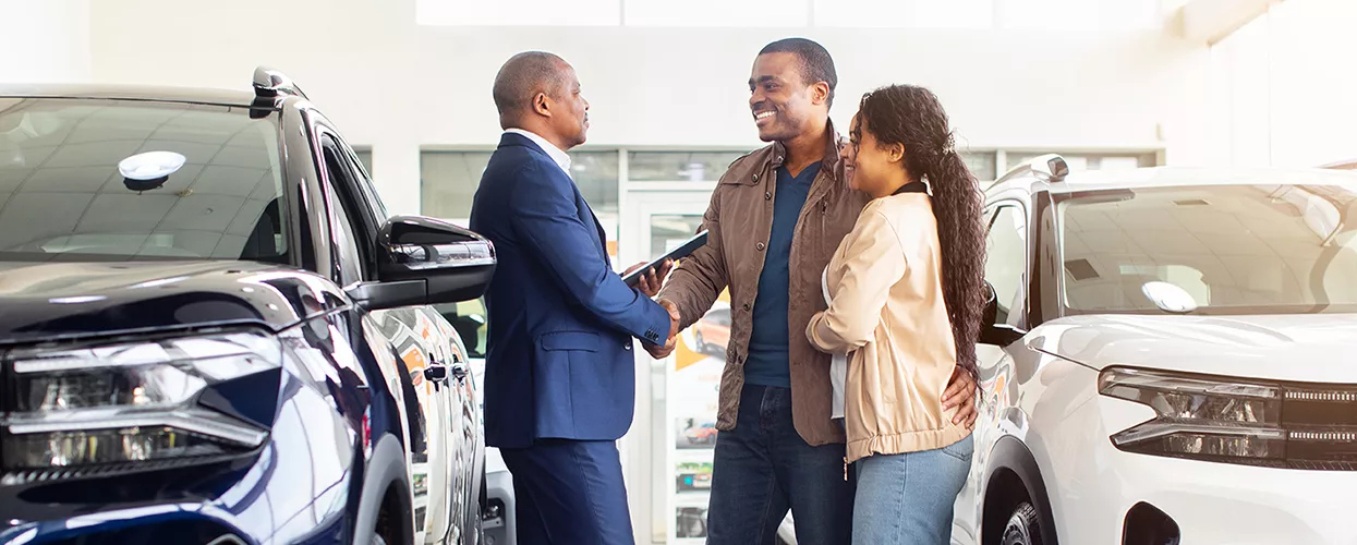 Happy customers shaking hands with a dealership sales consultant after purchasing a new SUV in a modern showroom