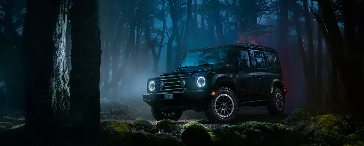 a INEOS Grenadier Trialmaster driving at night in a dark forest