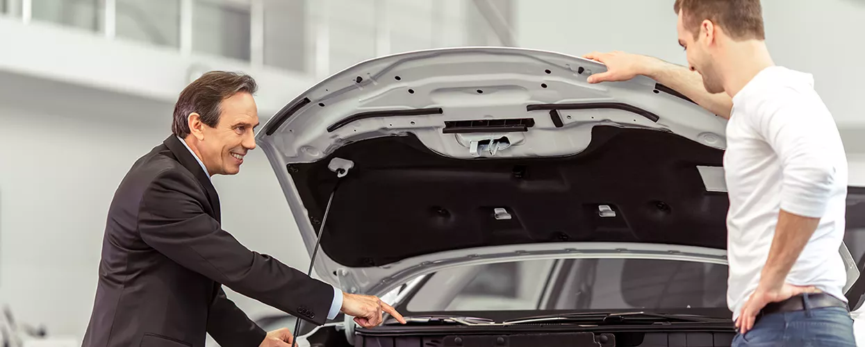 Car salesman showing a customer a car with the hood up
