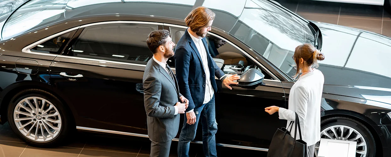 Two people are standing in front of a vehicle, seemingly in a casual discussion.