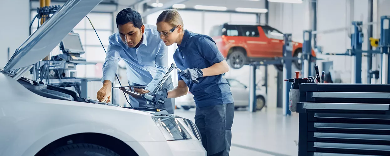 Two service mechanics working under the hood of a vehicle