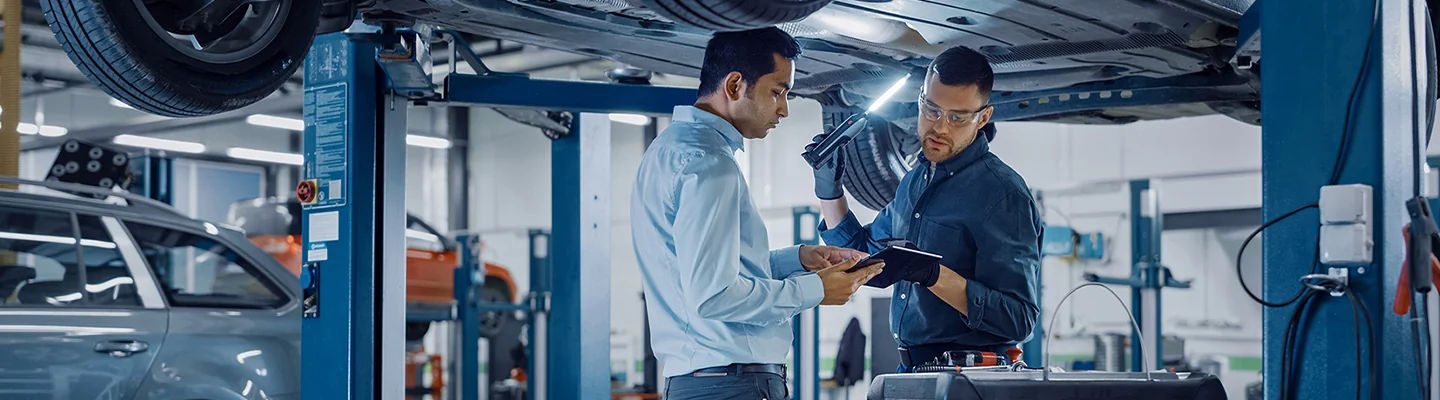 tech and mechanic looking over diagnosis report under a vehicle
