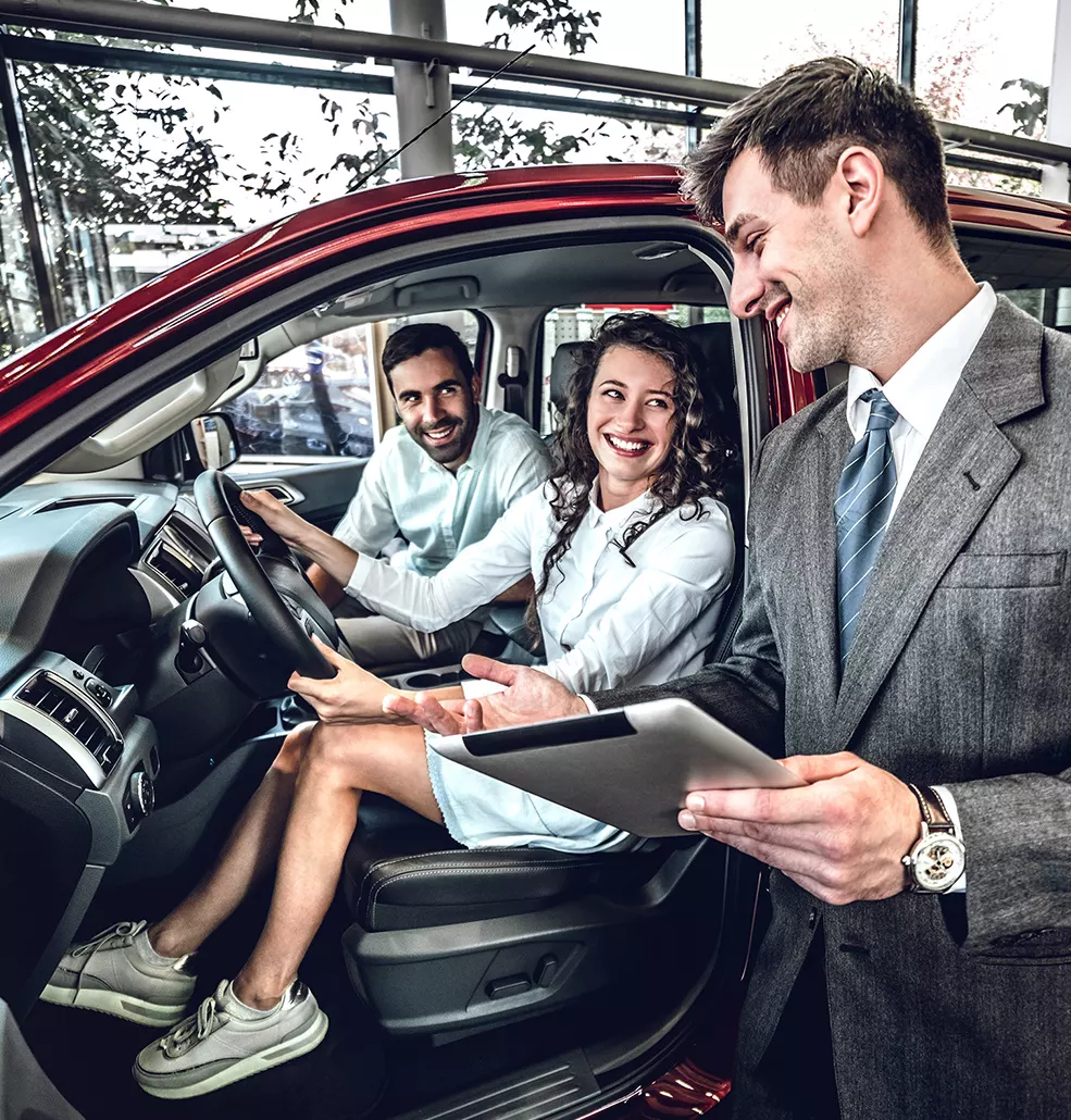 smiling sales agent helping 2 smiling customers inside car showroom