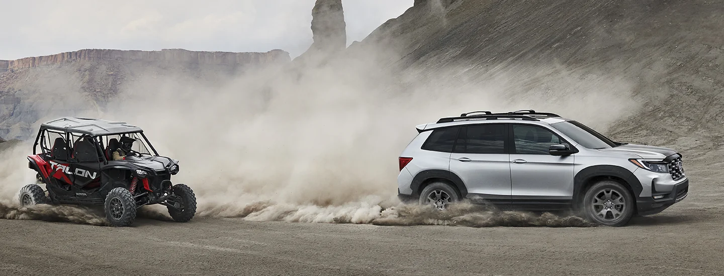 A gray 2025 Honda Passport driving in dirt with a 4-wheeler