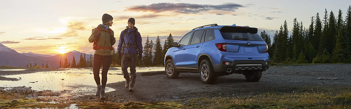 A blue 2025 Honda Passport parked with 2 people about to go on a hike