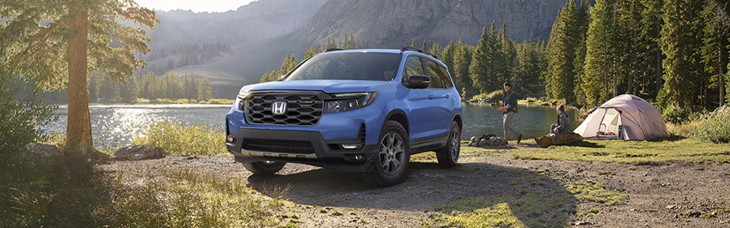Blue 2025 Honda Passport parked by a lake with people camping