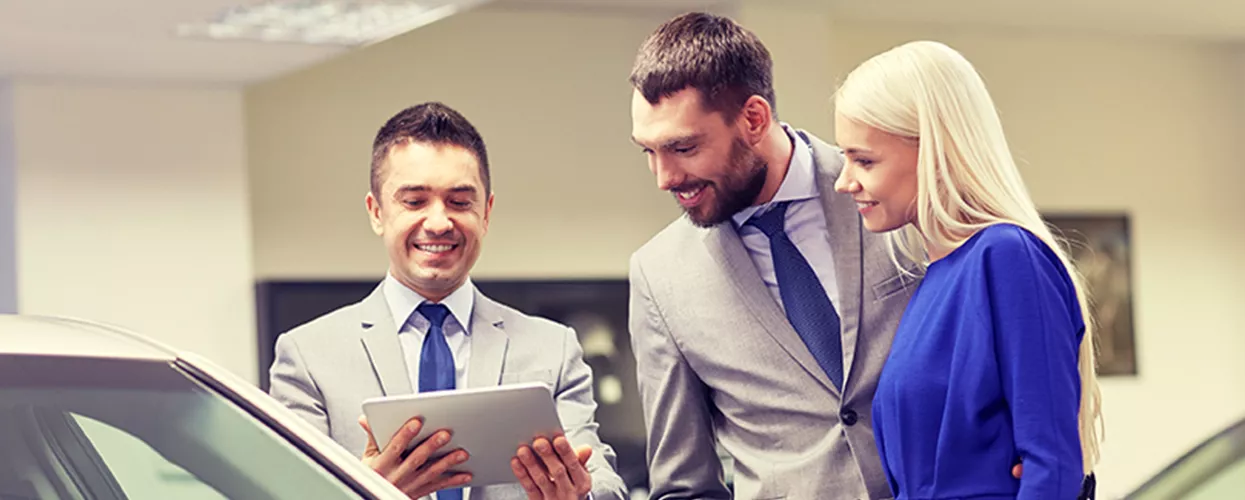 Car salesman showing a couple a tablet in a car dealership