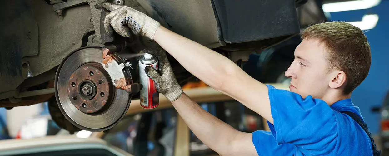 Technician inspecting brake pads on a Kia vehicle in a service bay