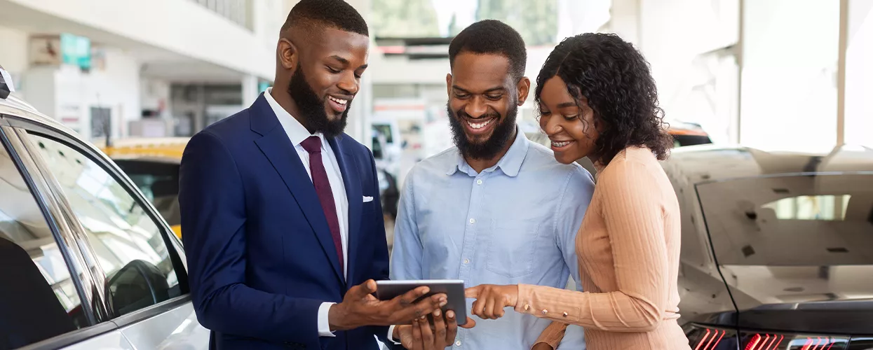 Car salesman talking to a couple and showing them something on a tablet