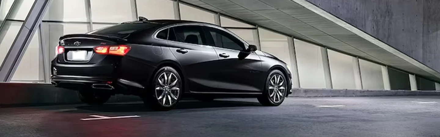 BAck side view of a parked 2024 Chevrolet Malibu in front of a building