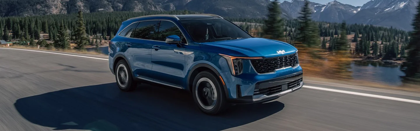 Blue 2025 Kia Sorento Hybrid driving by a lake and woods