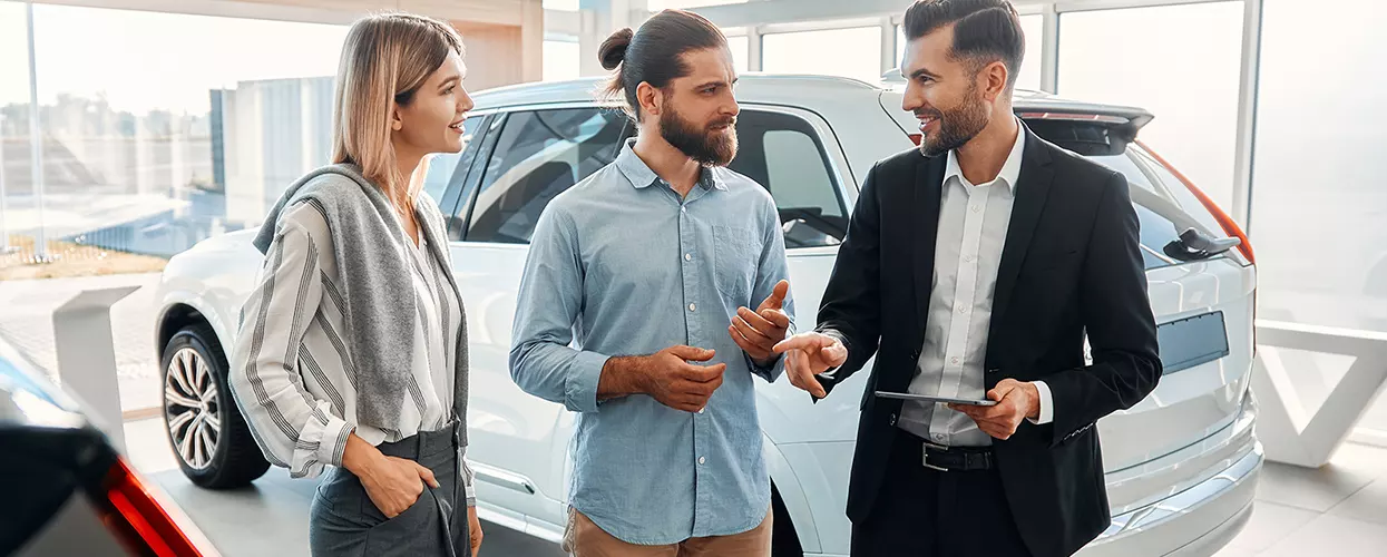 Car salesman talking to two people at a car dealership