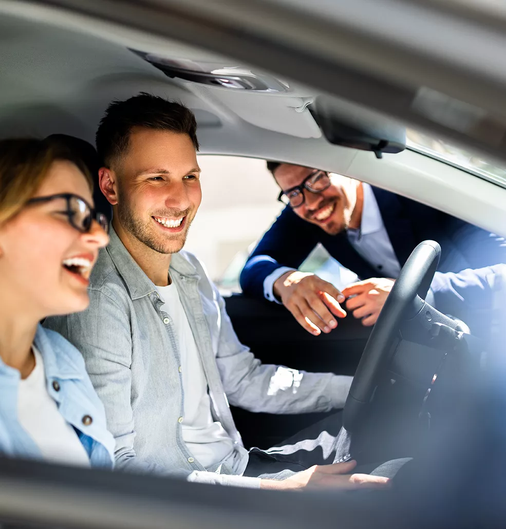 Couple sitting inside a new Kia with a car salesman standing outside