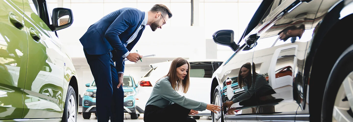 people looking at wheel of new car in showroom