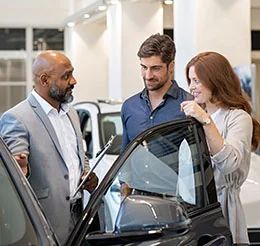 A couple discussing car details in the dealership showroom with a car salesperson