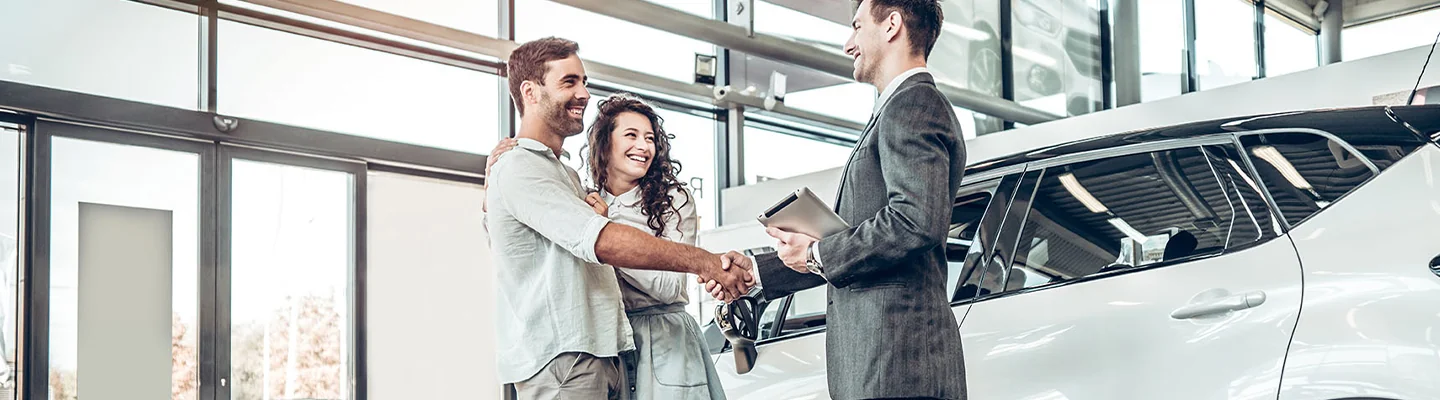 couple saking hands with car salesmen in suit