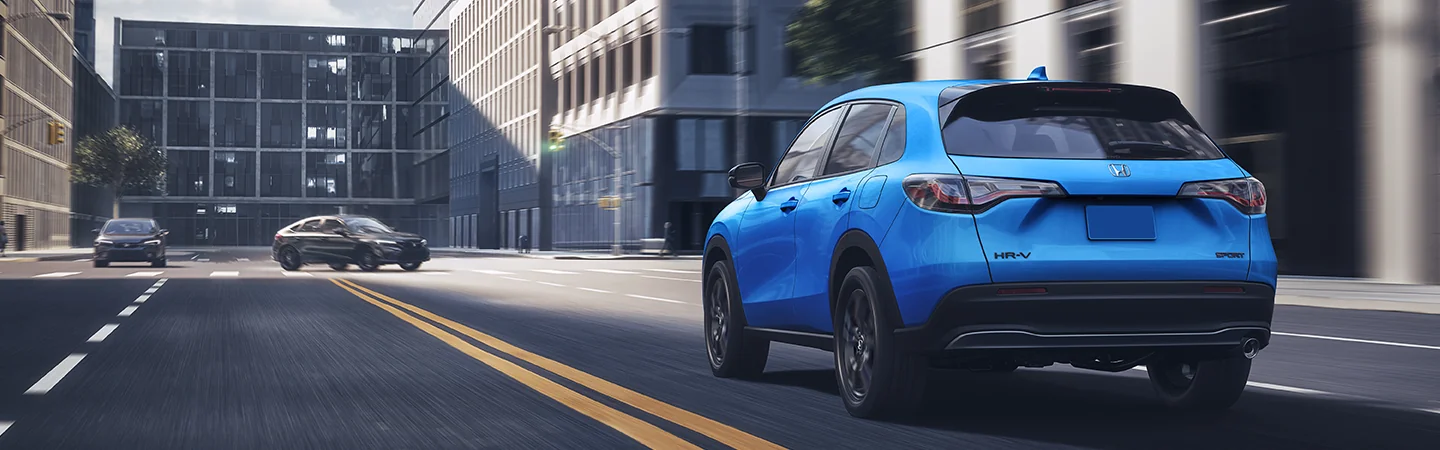 Back view of a blue 2026 Honda HR-V driving on a downtown city street