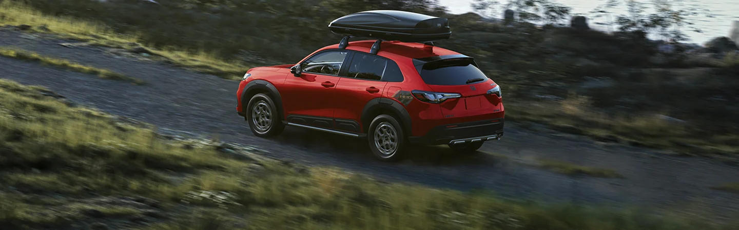 Back side view of a red 2026 Honda HR-V driving on a dirt road with a storage rack