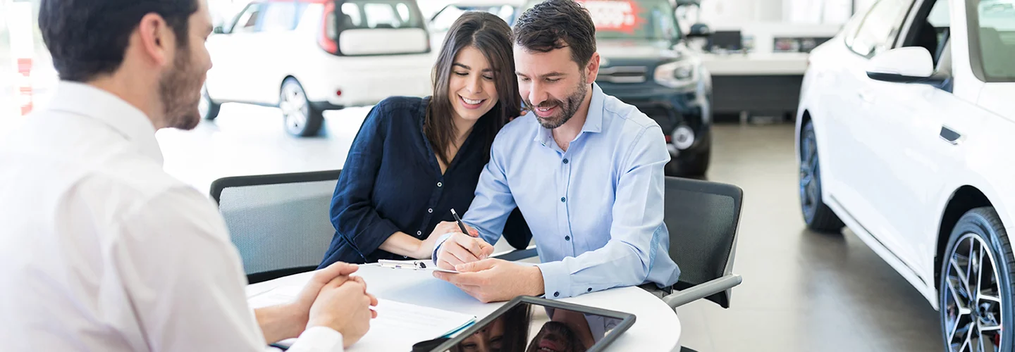 A man and woman sitting at a table in a car dealership, engaged in conversation about purchasing a vehicle.
