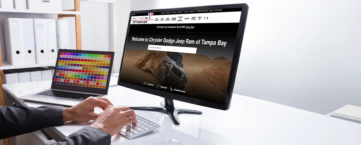 A man is focused on typing at a computer, where a car image is visible on the monitor.