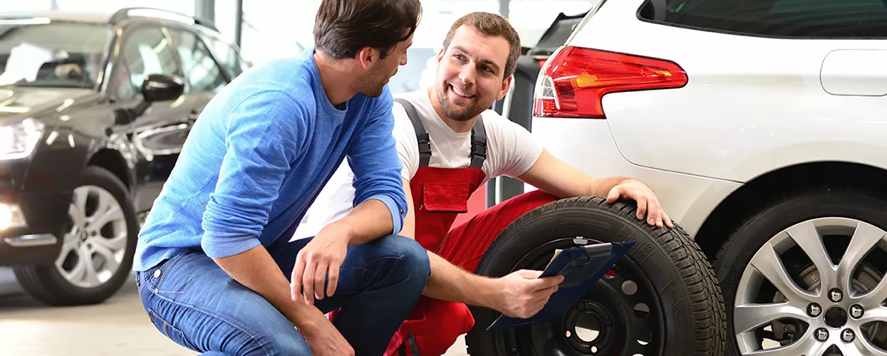 Automotive service technician discussing tire replacement and vehicle maintenance with a customer at a dealership service center
