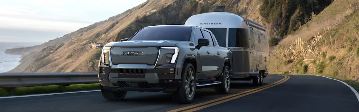 A gray 2024 GMC Sierra EV Denali Edition 1 pulling a trailer down the road