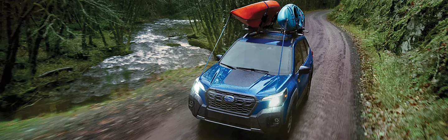 Blue 2024 Subaru Forester Wilderness driving on a trail next to a river