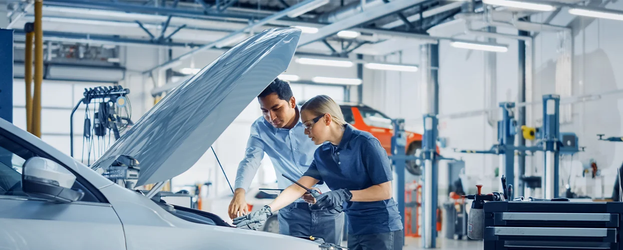 Two men collaborating on car maintenance in a garage, with tools and parts visible around them.