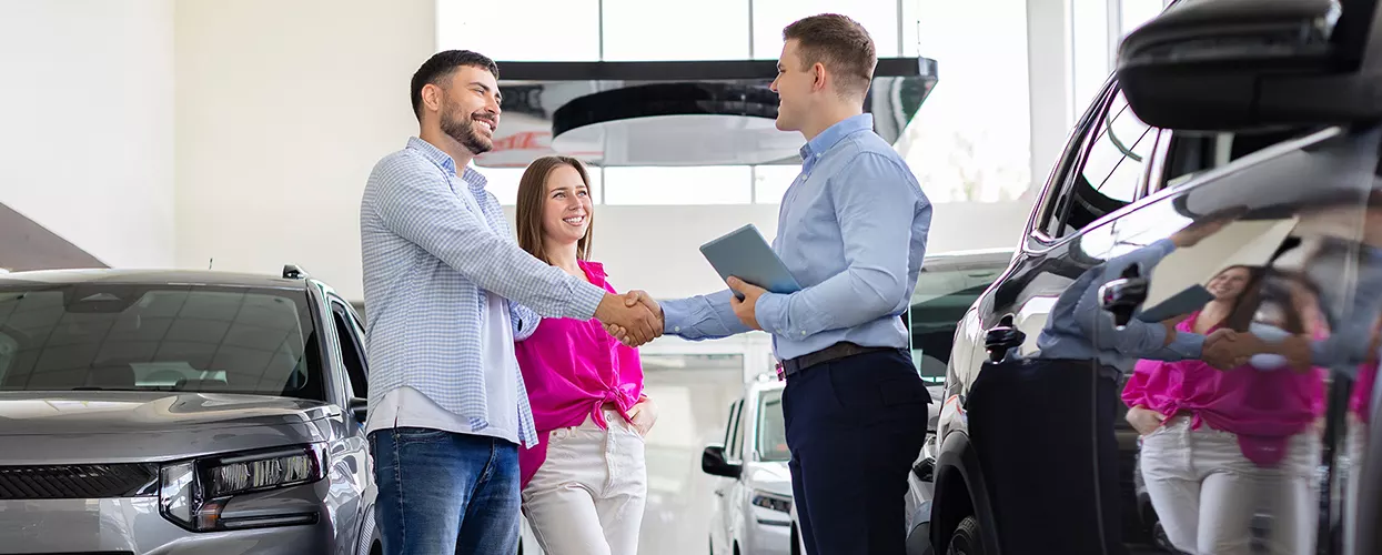 Couple with one shaking hands with car salesperson in showroom