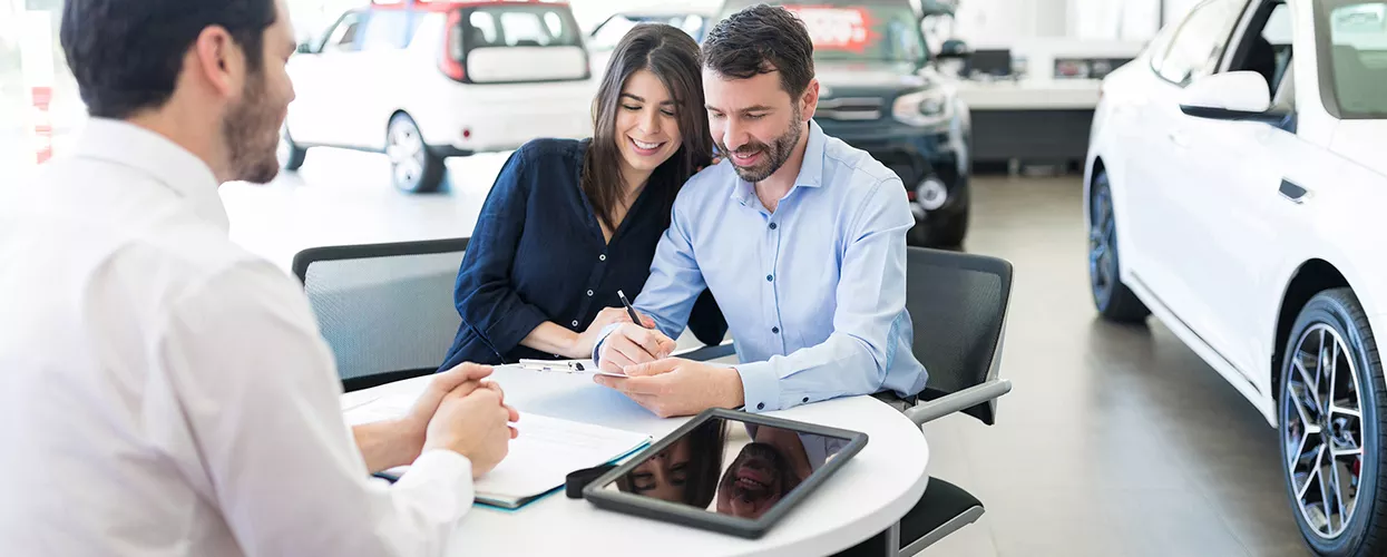 Couple sitting down and signing a document at a car dealership