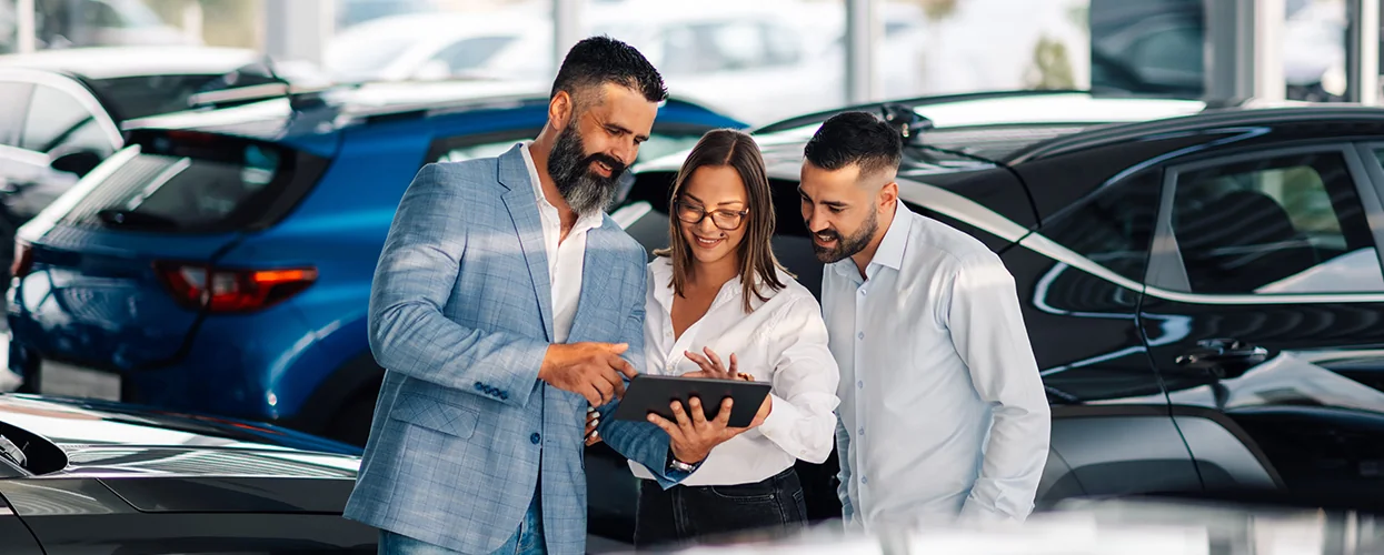 A group of three people inspecting a vehicle in a dealership, engaged in conversation about its specifications.