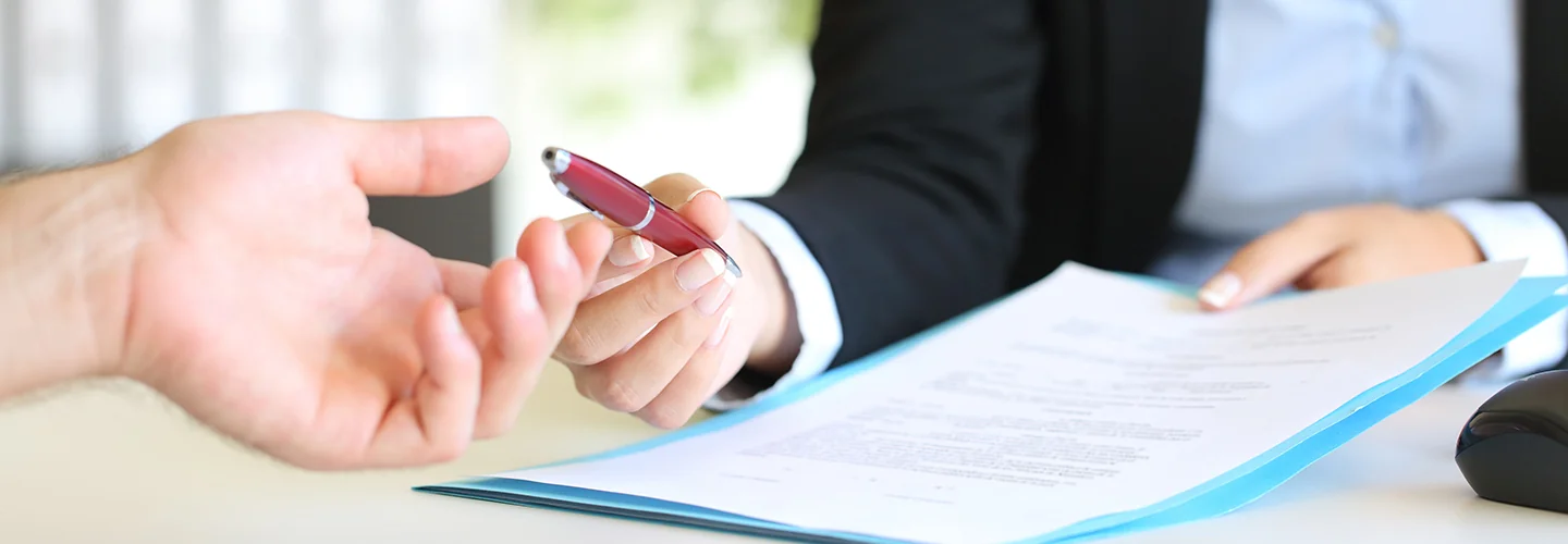 One person handing a pen to another to sign paperwork