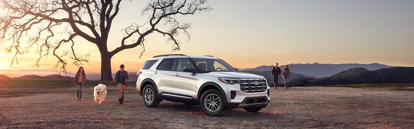 Front side view of a parked gray 2025 Ford Explorer with a family walking back after a hike