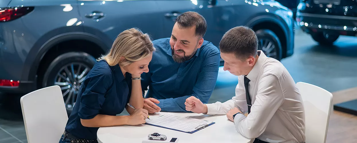 couple at a table with car salesperson going over a finance application to purchase a car