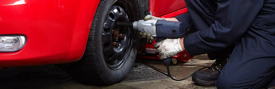 Automotive technician using an impact wrench to remove a vehicle tire during wheel and tire service in an auto repair shop